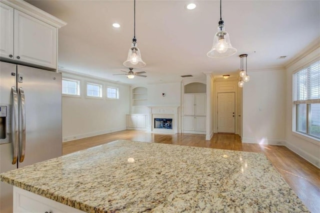 kitchen featuring stainless steel refrigerator with ice dispenser, built in shelves, hanging light fixtures, and white cabinets