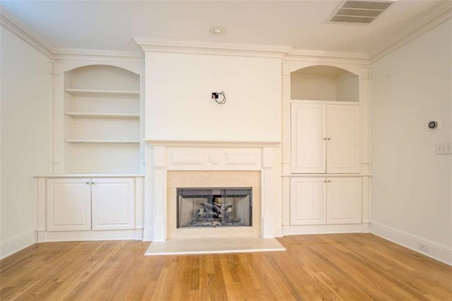 unfurnished living room featuring crown molding, built in features, and light wood-type flooring