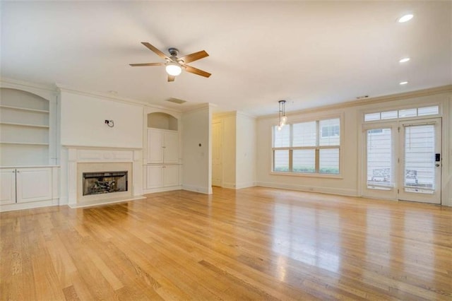 unfurnished living room with crown molding, built in shelves, ceiling fan, and light hardwood / wood-style flooring