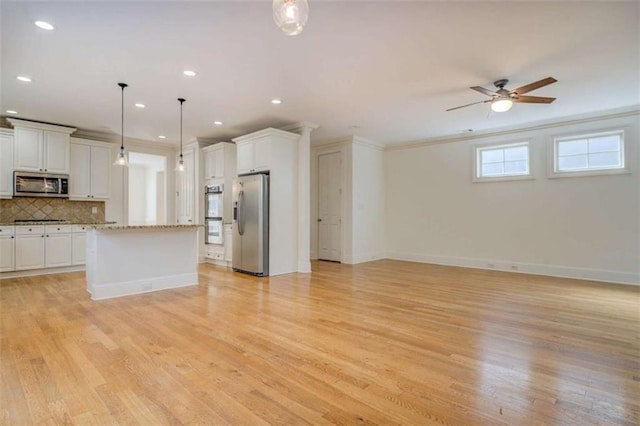 kitchen featuring decorative light fixtures, white cabinetry, a center island, stainless steel appliances, and light stone countertops