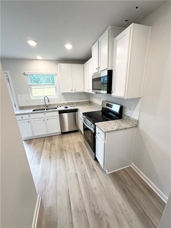 kitchen with sink, white cabinetry, stainless steel appliances, light stone countertops, and decorative backsplash