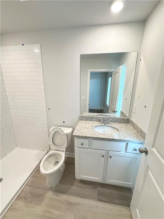 bathroom with vanity, tiled shower, hardwood / wood-style floors, and toilet