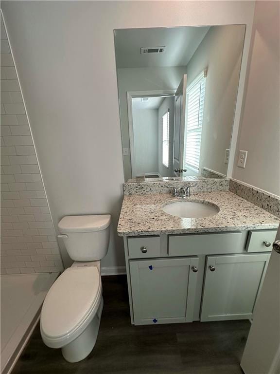 bathroom featuring vanity, hardwood / wood-style floors, toilet, and a tile shower