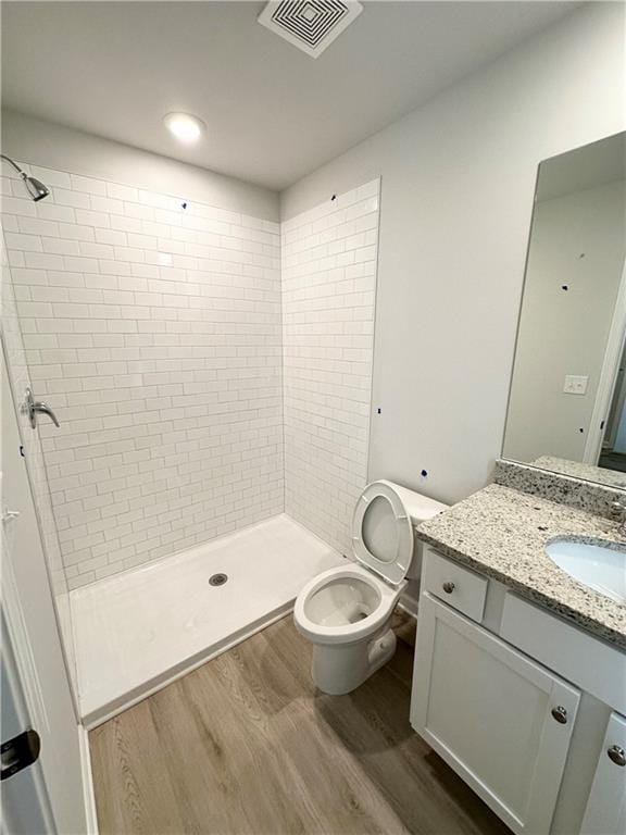 bathroom featuring hardwood / wood-style flooring, tiled shower, vanity, and toilet