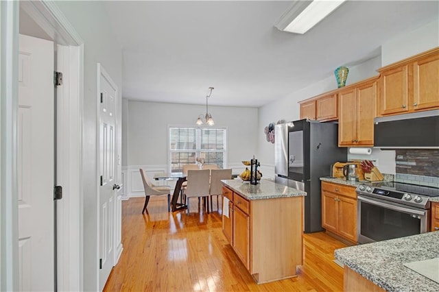 kitchen featuring light stone countertops, light wood-style floors, appliances with stainless steel finishes, and a wainscoted wall