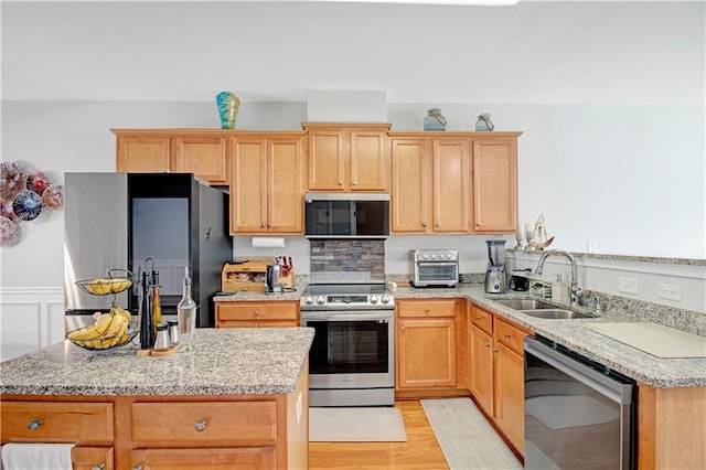 kitchen with light wood-style flooring, stainless steel appliances, a sink, a center island, and light brown cabinetry