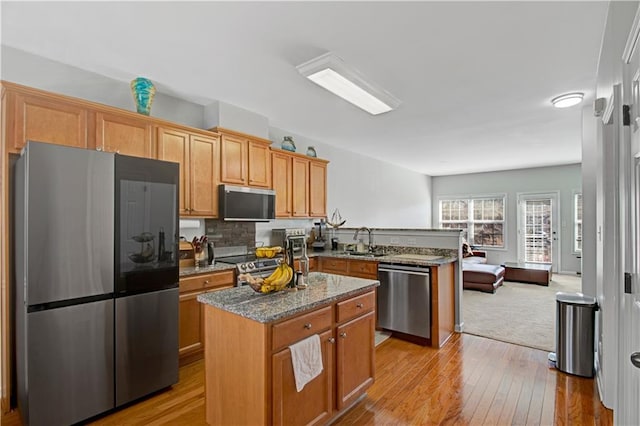 kitchen with dark stone countertops, a peninsula, stainless steel appliances, light wood-type flooring, and a sink