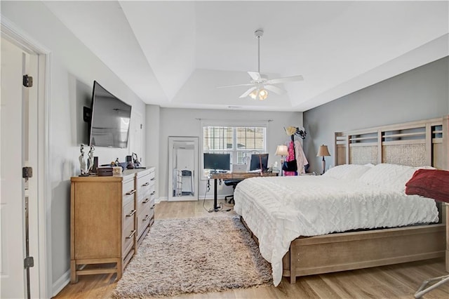 bedroom featuring light wood-type flooring, baseboards, a tray ceiling, and ceiling fan