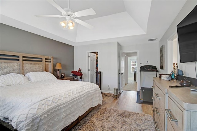 bedroom with baseboards, visible vents, a raised ceiling, a ceiling fan, and light wood-type flooring