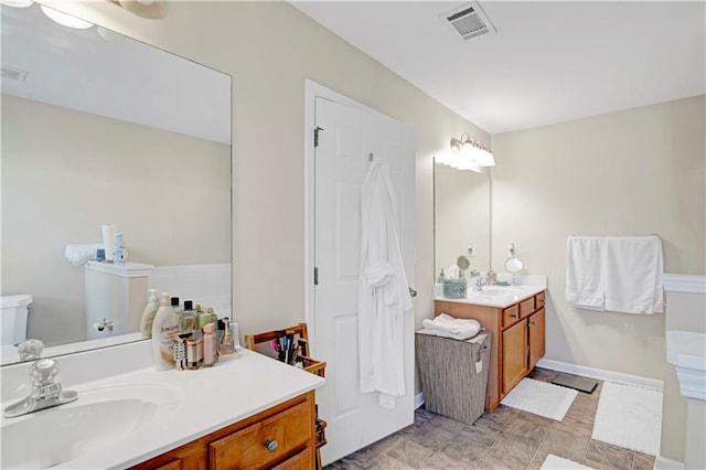 full bath featuring two vanities, a sink, visible vents, and baseboards