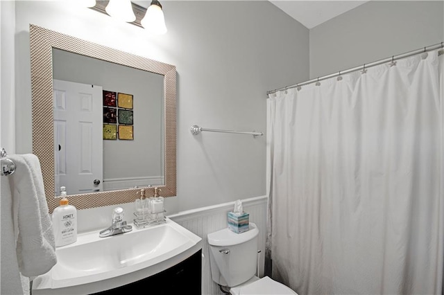 full bath with curtained shower, wainscoting, vanity, and toilet