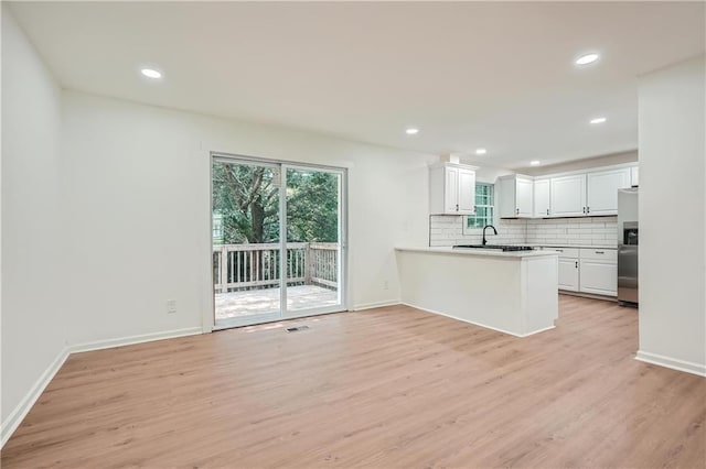 kitchen with kitchen peninsula, decorative backsplash, stainless steel refrigerator with ice dispenser, light wood-type flooring, and white cabinetry