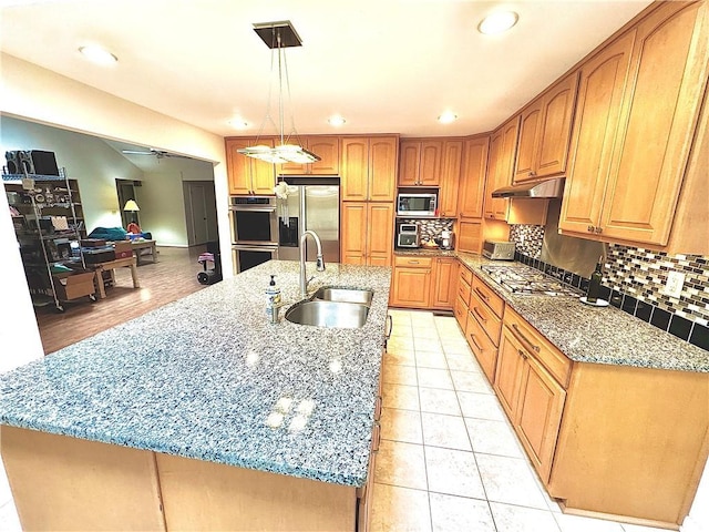 kitchen featuring light stone countertops, under cabinet range hood, stainless steel appliances, a sink, and decorative backsplash