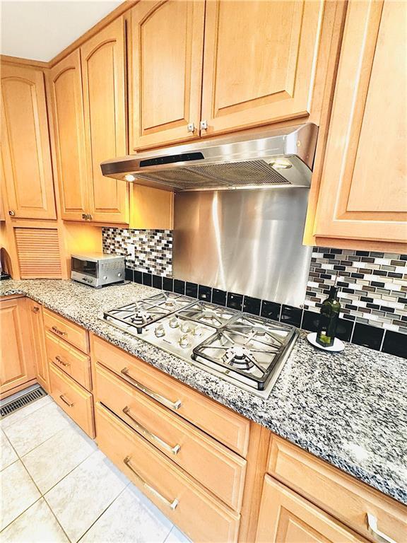 kitchen featuring light tile patterned flooring, stainless steel gas cooktop, under cabinet range hood, and light brown cabinetry