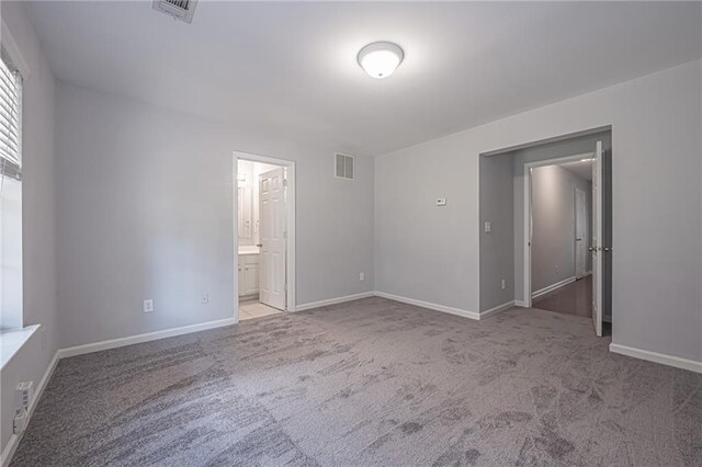 unfurnished bedroom featuring light colored carpet and connected bathroom