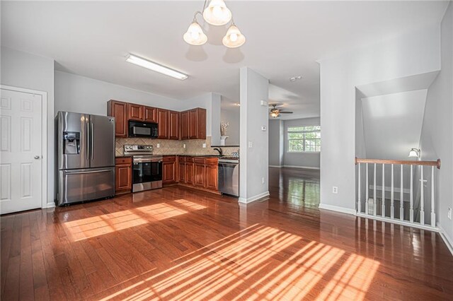 kitchen with decorative light fixtures, backsplash, dark wood-type flooring, appliances with stainless steel finishes, and ceiling fan with notable chandelier