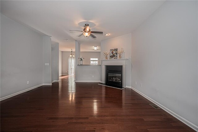 unfurnished living room with ceiling fan with notable chandelier and dark wood-type flooring