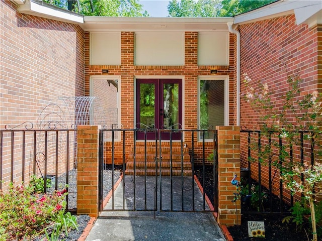 entrance to property with a gate, french doors, brick siding, and fence