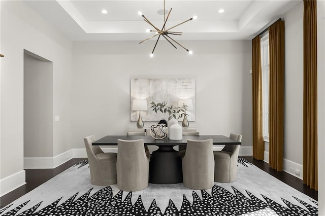 dining space featuring dark hardwood / wood-style flooring, a raised ceiling, and a notable chandelier