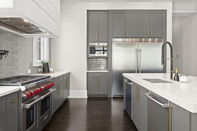 kitchen with decorative backsplash, premium appliances, wall chimney range hood, and gray cabinets