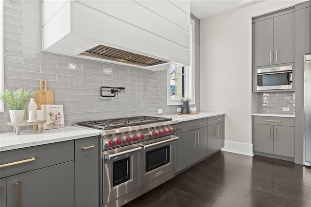 kitchen with gray cabinets, backsplash, custom range hood, range with two ovens, and light stone countertops