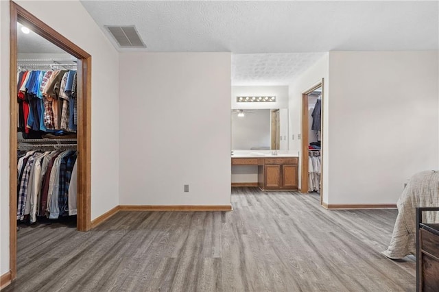 unfurnished bedroom with baseboards, light wood finished floors, visible vents, a spacious closet, and a closet