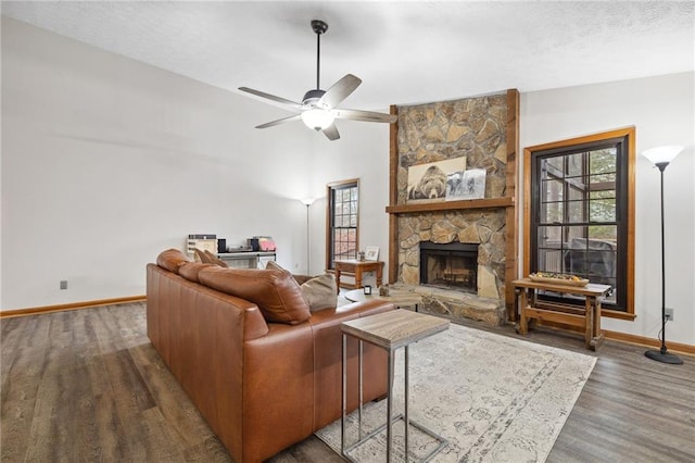 living area featuring wood finished floors, baseboards, ceiling fan, a stone fireplace, and a textured ceiling