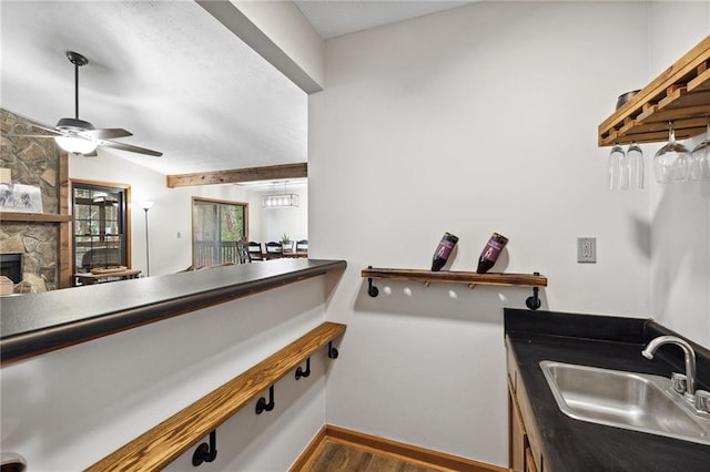 kitchen with lofted ceiling, a fireplace, wood finished floors, a ceiling fan, and a sink