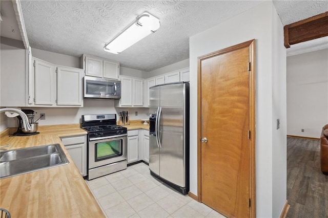 kitchen featuring light tile patterned floors, a sink, stainless steel appliances, white cabinets, and a textured ceiling