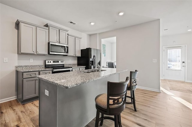 kitchen with light stone countertops, appliances with stainless steel finishes, gray cabinets, and a center island with sink