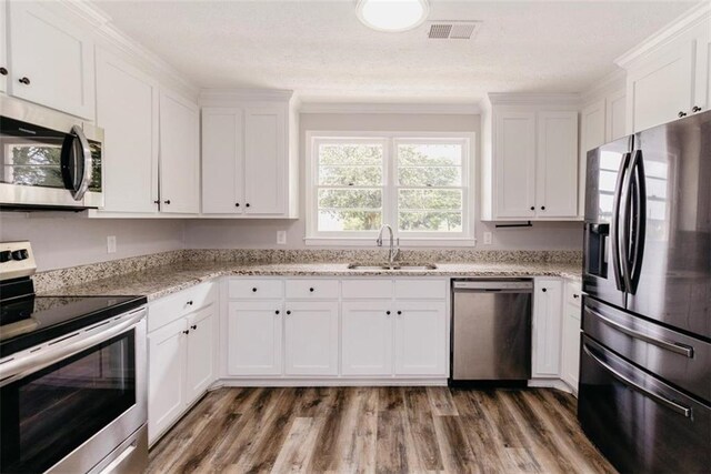 1233 Bethlehem Rd, Statham, GA 30666 - kitchen with stainless steel appliances, a sink, white cabinets, wood finished floors, and light stone counters