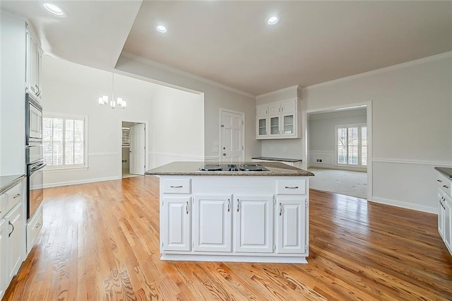 kitchen with ornamental molding, a center island, stovetop, white cabinets, and a chandelier