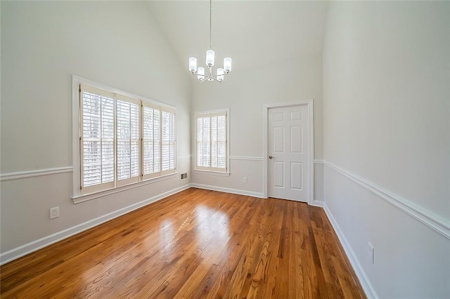 empty room with an inviting chandelier, wood finished floors, baseboards, and high vaulted ceiling