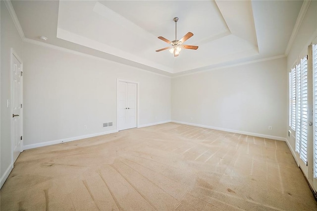 empty room with a raised ceiling, light colored carpet, visible vents, and baseboards