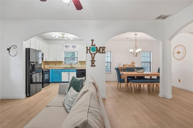 living room with baseboards, visible vents, light wood finished floors, and ceiling fan with notable chandelier