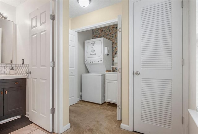 washroom featuring a textured ceiling, baseboards, stacked washer / drying machine, and light colored carpet