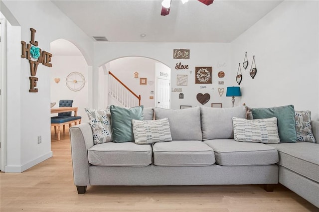 living area with arched walkways, ceiling fan, visible vents, and light wood-style flooring