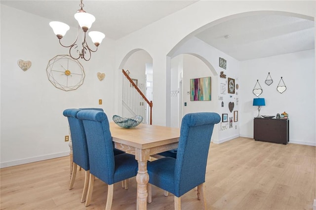 dining space featuring arched walkways, a notable chandelier, baseboards, stairs, and light wood-style floors