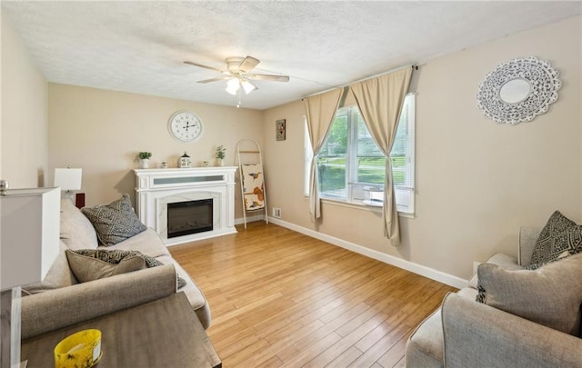 living room featuring wood finished floors, a ceiling fan, a high end fireplace, baseboards, and a textured ceiling