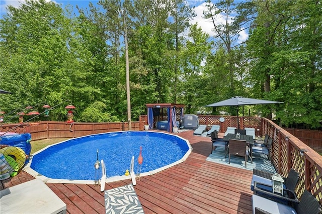 view of swimming pool featuring a wooden deck, a fenced backyard, outdoor dining area, and view of scattered trees