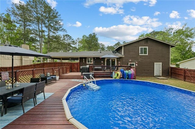view of swimming pool featuring a wooden deck, a fenced backyard, and outdoor dining space