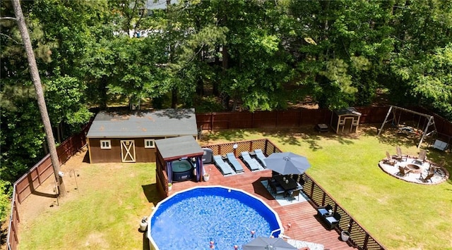 view of swimming pool featuring a wooden deck, an outdoor structure, outdoor dining space, an outdoor fire pit, and view of wooded area