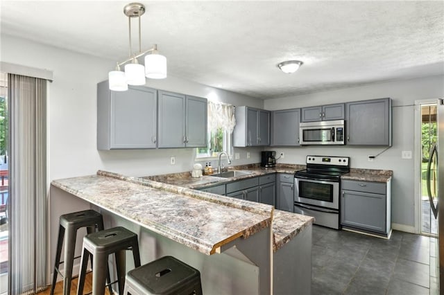 kitchen featuring stainless steel appliances, a sink, plenty of natural light, a peninsula, and a textured ceiling