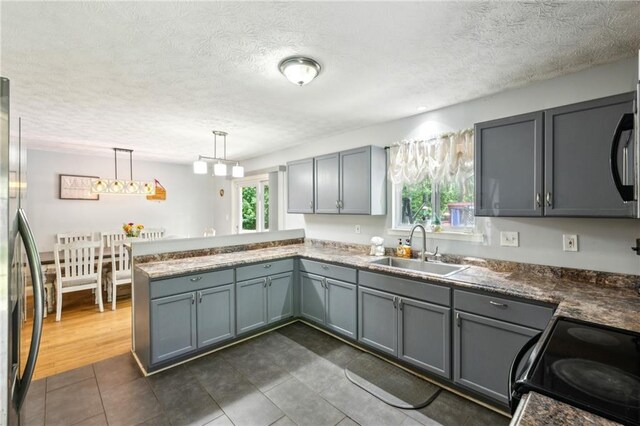 kitchen featuring a sink, gray cabinetry, stainless steel fridge, black range with electric stovetop, and a peninsula