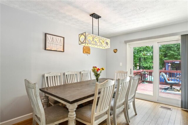 dining area with light wood finished floors, a textured ceiling, and baseboards