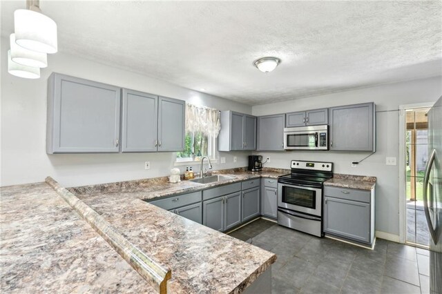 kitchen featuring appliances with stainless steel finishes, gray cabinetry, a sink, a textured ceiling, and a peninsula