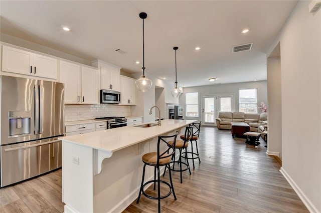 kitchen with sink, decorative light fixtures, appliances with stainless steel finishes, a kitchen island with sink, and white cabinets