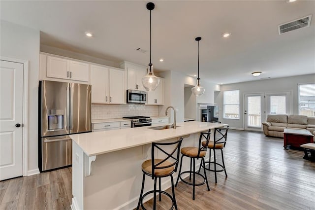 kitchen with white cabinetry, sink, hanging light fixtures, stainless steel appliances, and a center island with sink