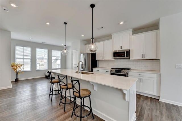 kitchen featuring white cabinetry, hanging light fixtures, an island with sink, and appliances with stainless steel finishes