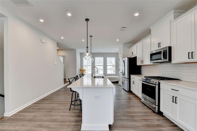 kitchen featuring a kitchen island with sink, white cabinetry, stainless steel appliances, tasteful backsplash, and decorative light fixtures